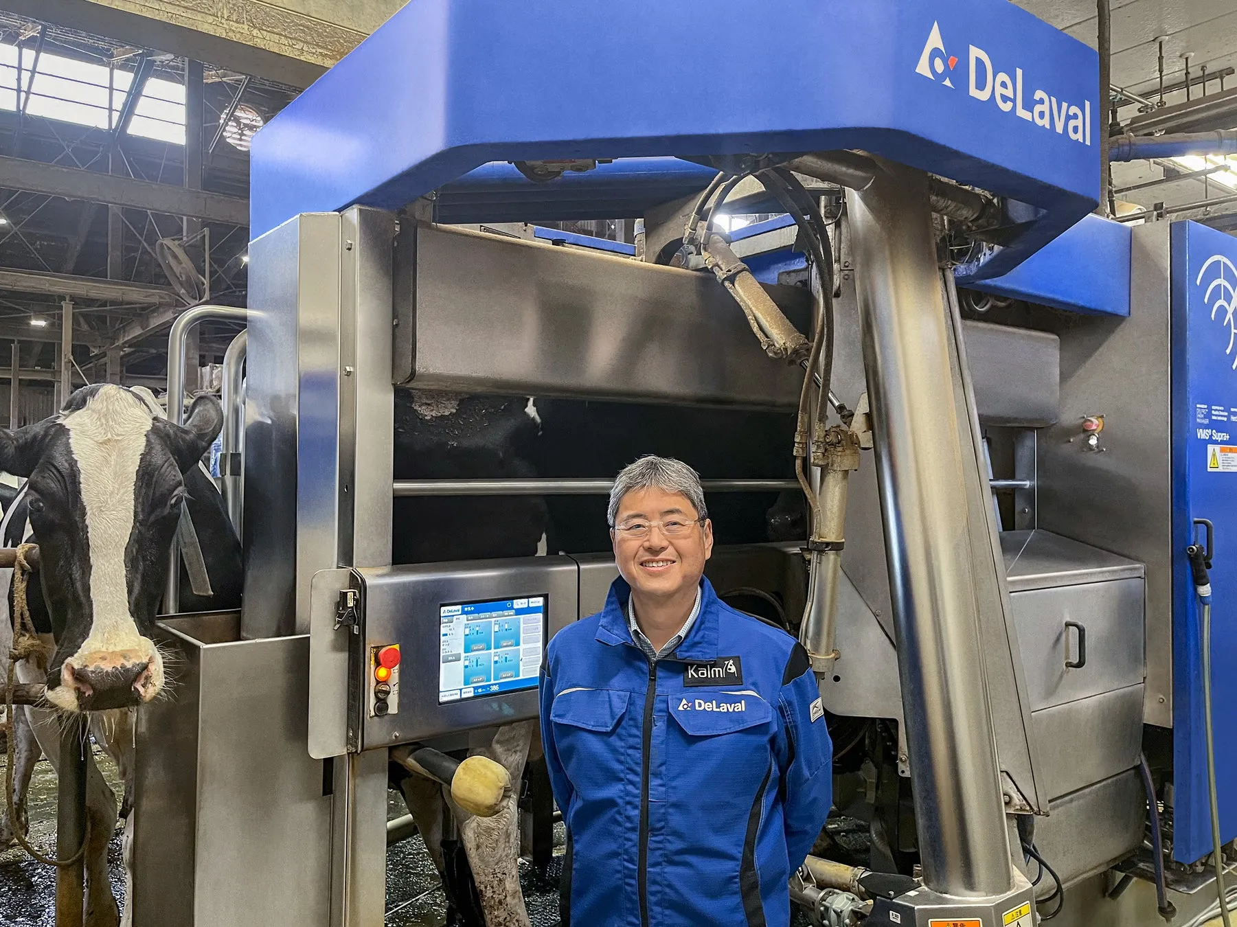 DeLavalの搾乳システムの前で笑顔の男性が立っており、牛がシステムの近くに立っています。