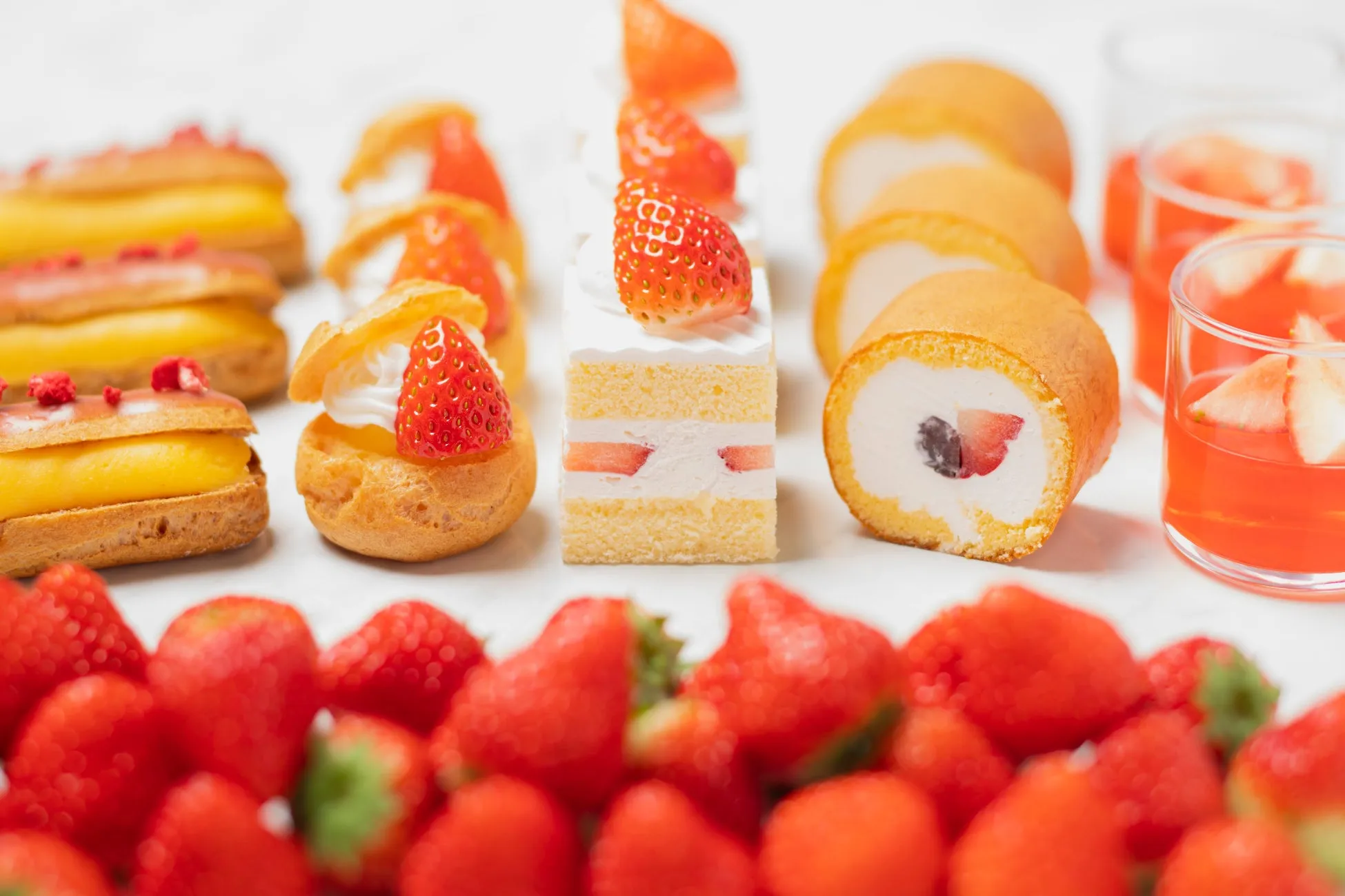 様々なデザートが並べられた写真。シュークリーム、エクレア、ケーキ、ロールケーキ、イチゴジュースなど、美味しそうなスイーツが並んでいる。