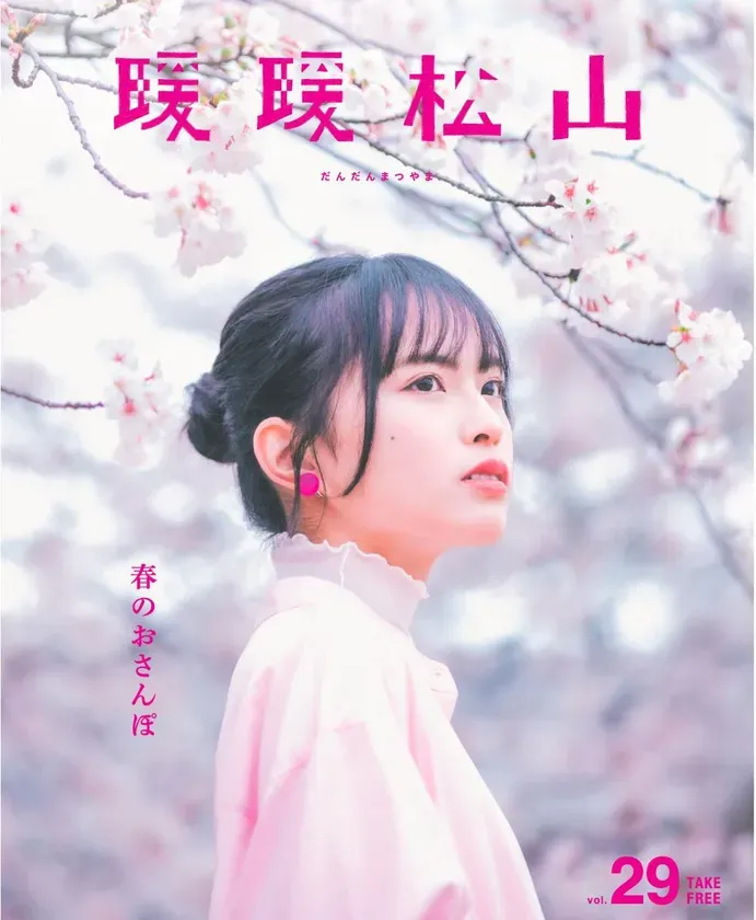 桜の木の下で横顔を見せる女性のポートレート。ピンク色の服を着ており、ピンク色のイヤリングをしている。背景には桜の花が咲き乱れている。