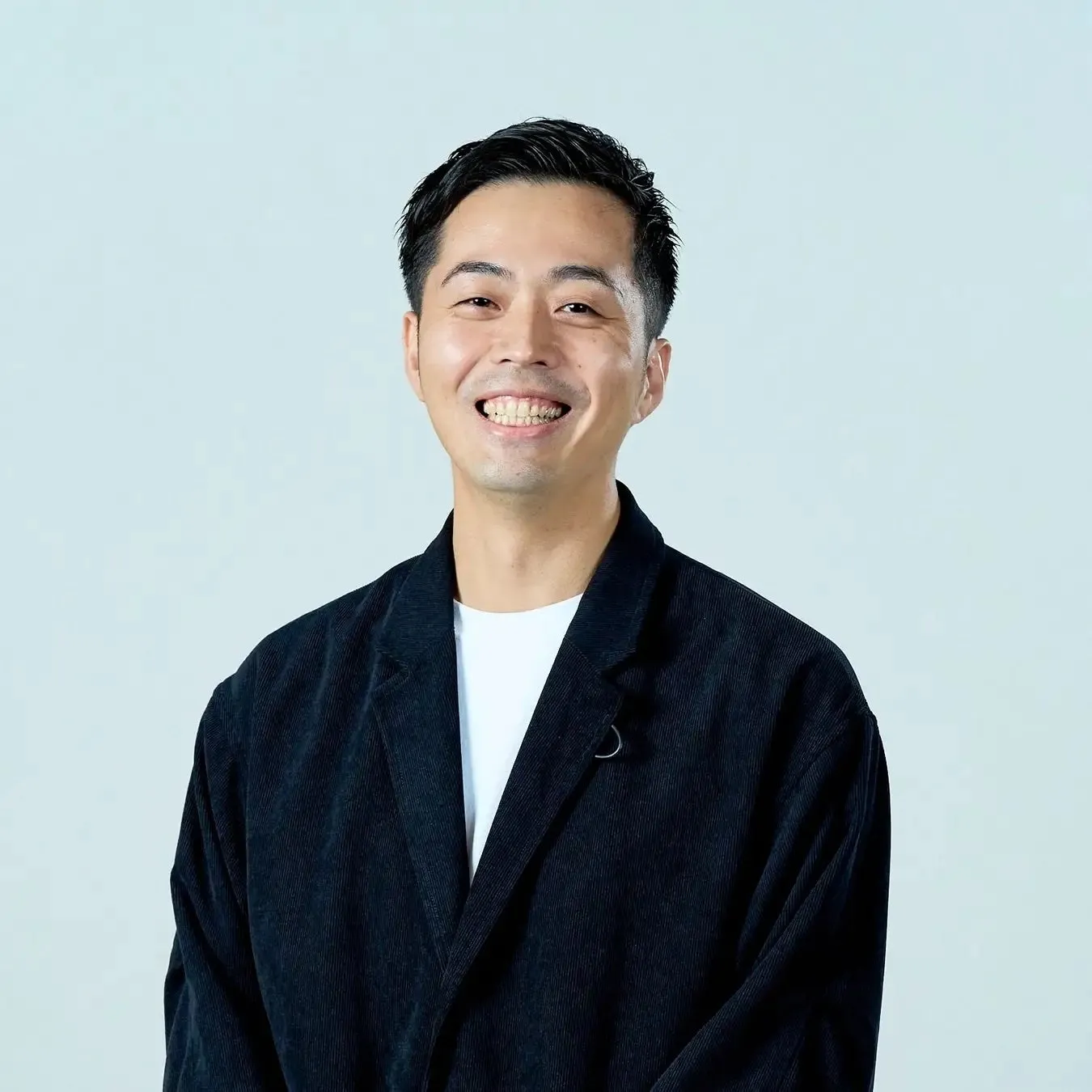 笑顔の男性のポートレート。彼は黒いジャケットと白いTシャツを着ていて、背景は白です。