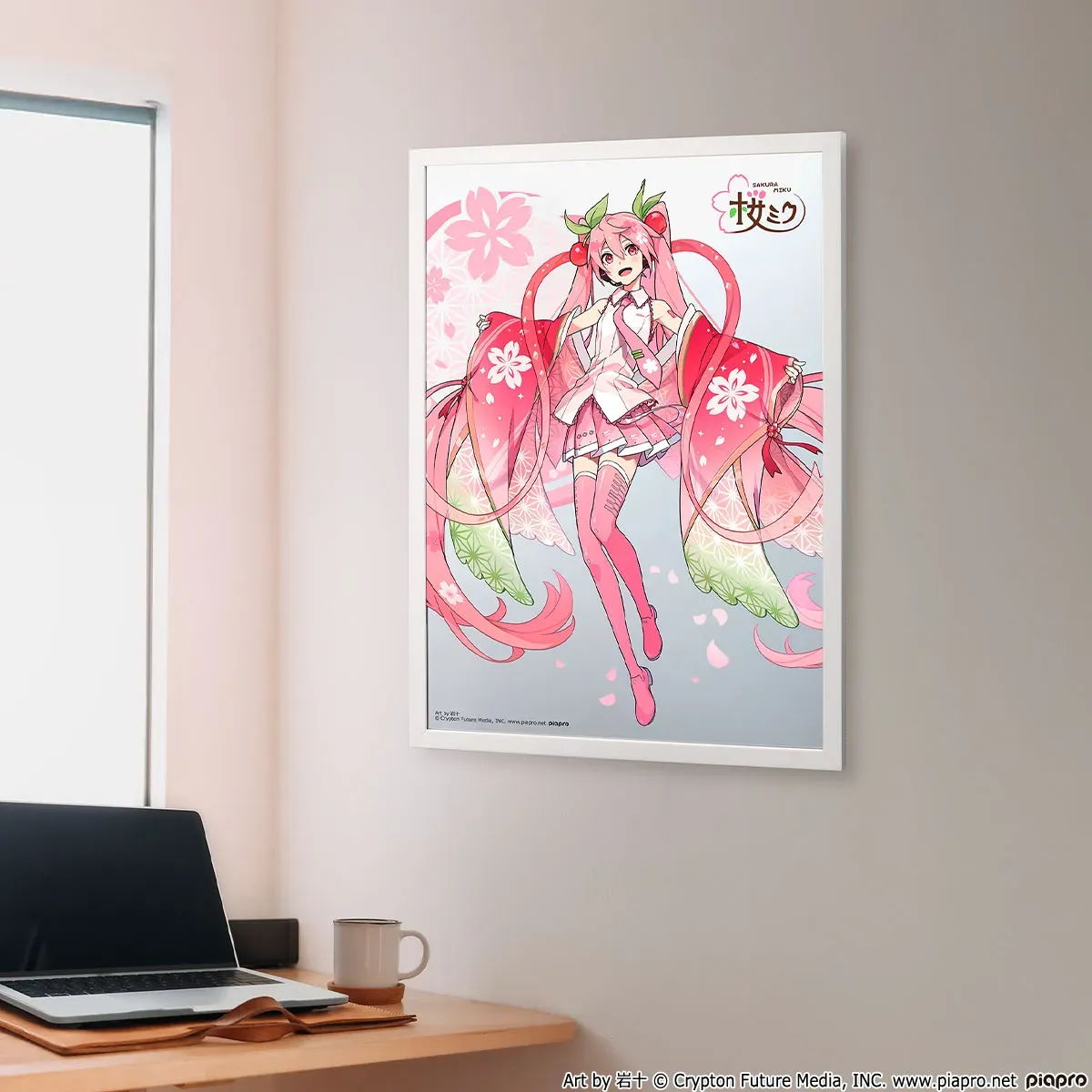 桜をテーマにしたイラストが飾られた部屋の写真。イラストには、ピンク色の髪と衣装を身に着けたキャラクターが描かれており、背景には桜の花びらが散っている。机の上にはノートパソコン、マグカップ、コースターが置かれている。