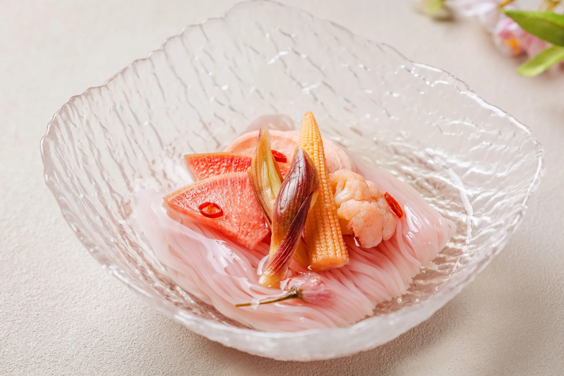 透明なガラスの器に盛られた、ピンク色の素麺と野菜の盛り合わせ。