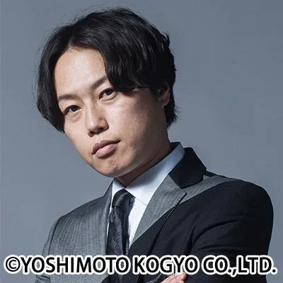 スーツを着た男性のポートレート写真です。彼はカメラ目線で、暗い背景に立っています。