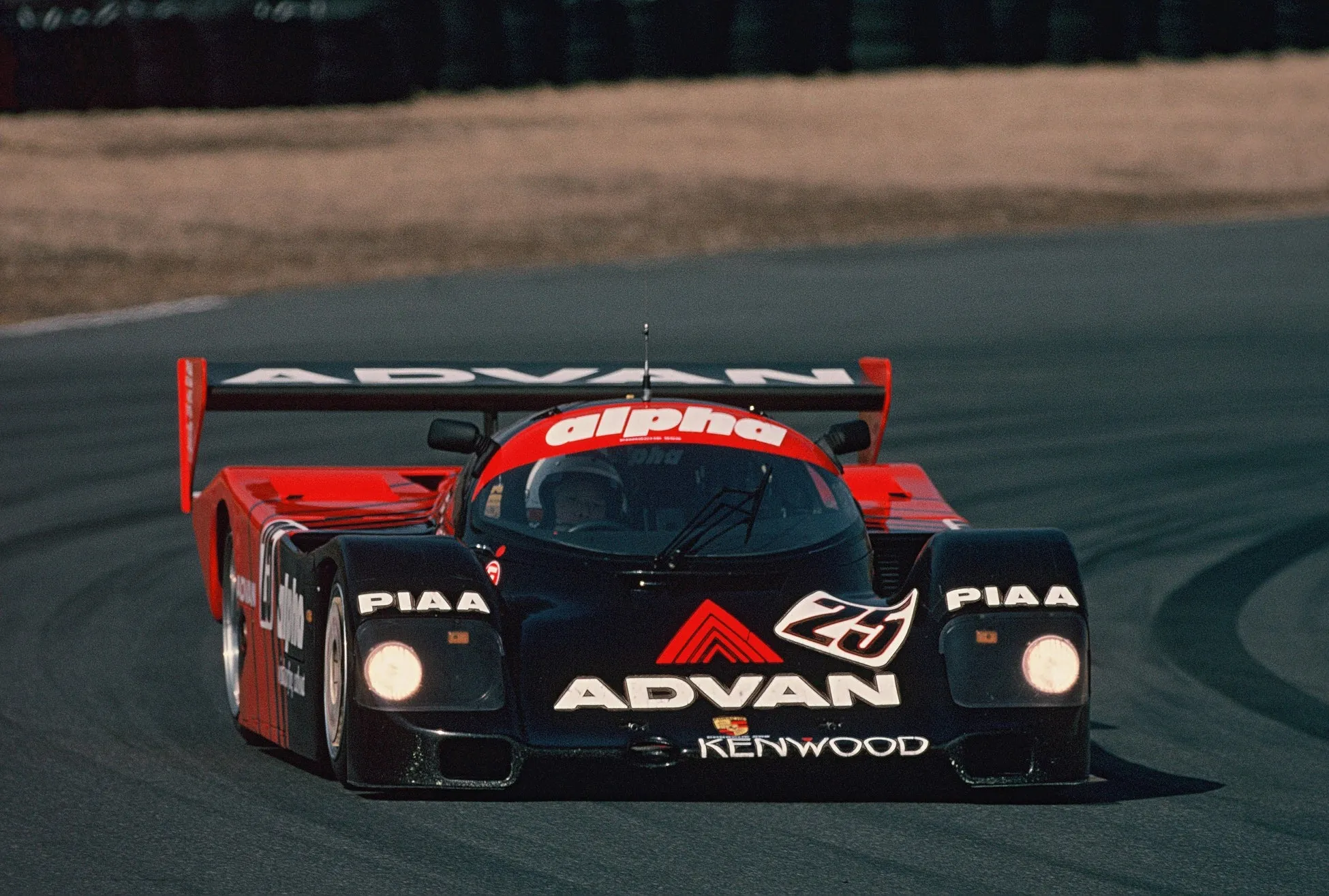 レース中の黒と赤のレーシングカーのクローズアップ写真。車には「alpha」、「PIAA」、「ADVAN」、「KENWOOD」という言葉が書かれており、ナンバー25が描かれています。