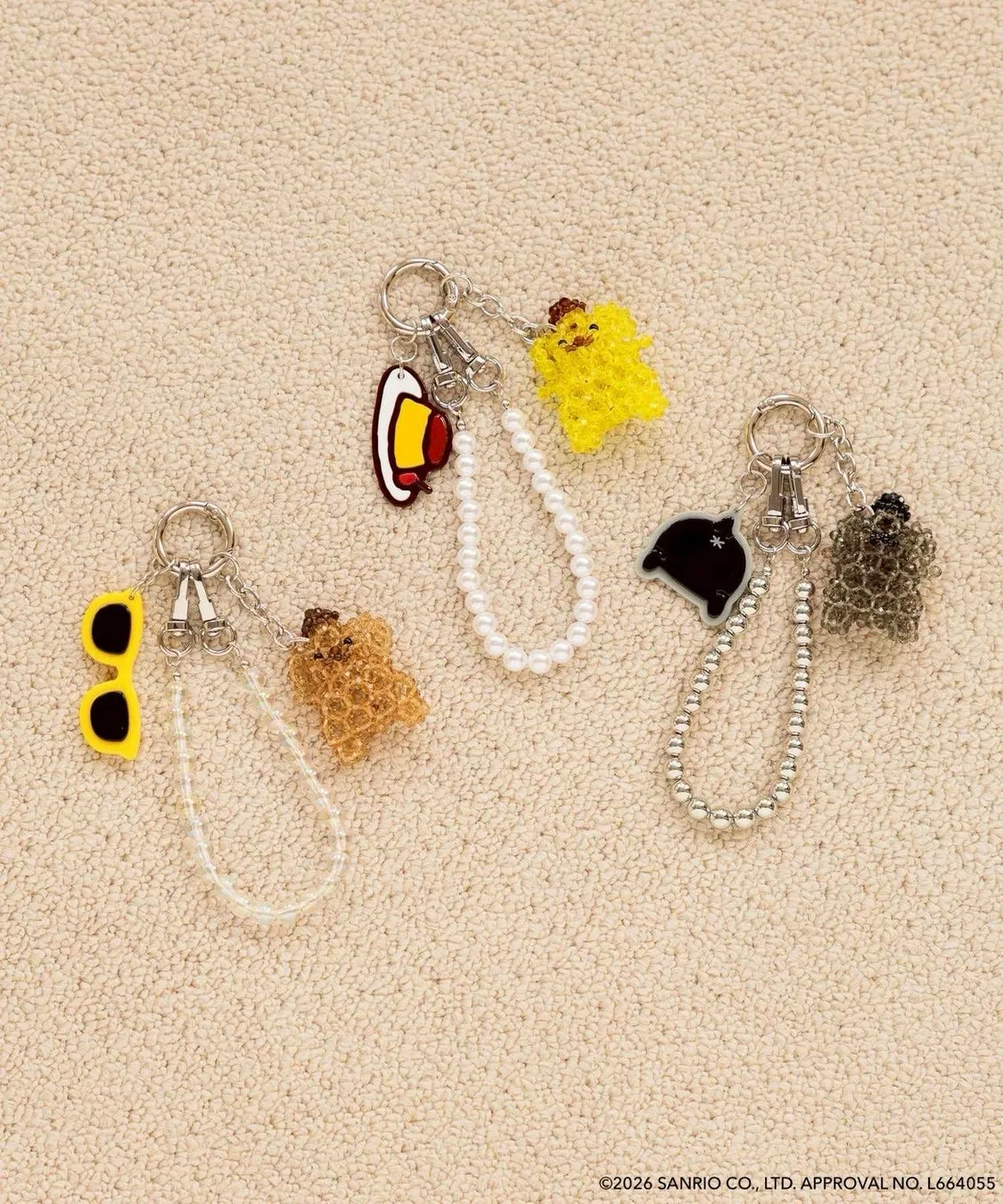 キーホルダーが3つ並んだ写真。キーホルダーはそれぞれ異なるデザインで、サングラス、クマ、ひよこ、ベル、リボンなどが装飾されている。キーホルダーはビーズやパールで装飾され、可愛らしい印象を与えている。
