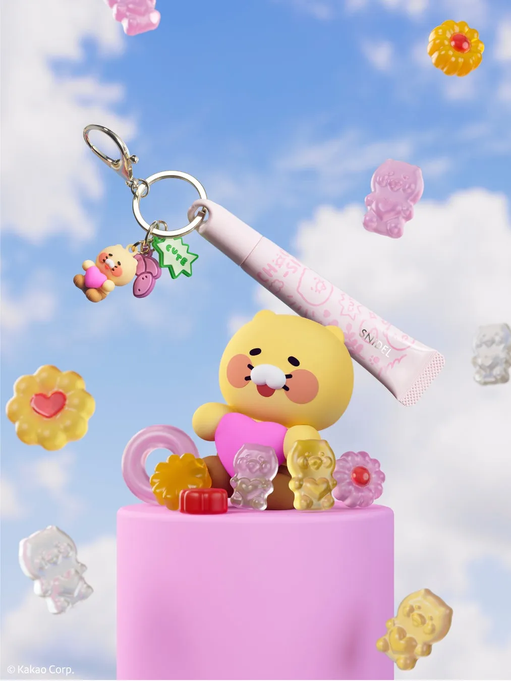 空を背景に、ピンク色の台座の上に可愛らしいキャラクターが配置された画像です。キャラクターは黄色いクマのようで、ピンク色のハートを抱いています。周りには様々な形をしたグミや、リップクリーム、キーホルダーなどが配置されています。全体的にポップでキュートな印象です。