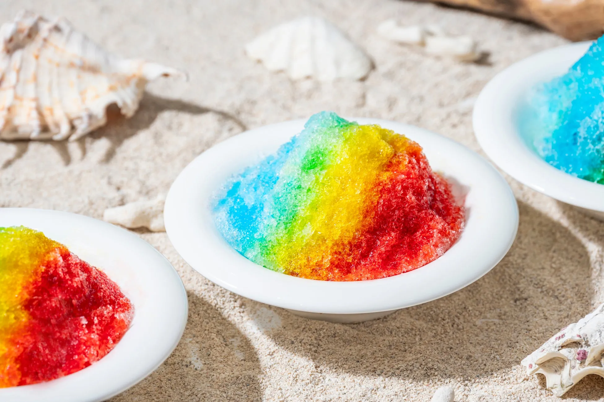 カラフルなかき氷が白いお皿に盛られ、砂浜に置かれている写真