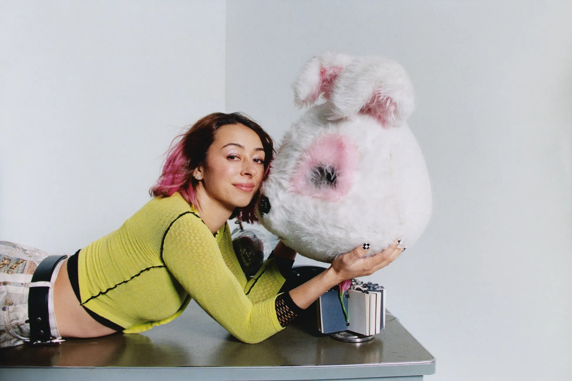 ピンクの髪の女性が白いウサギのぬいぐるみと寄り添う