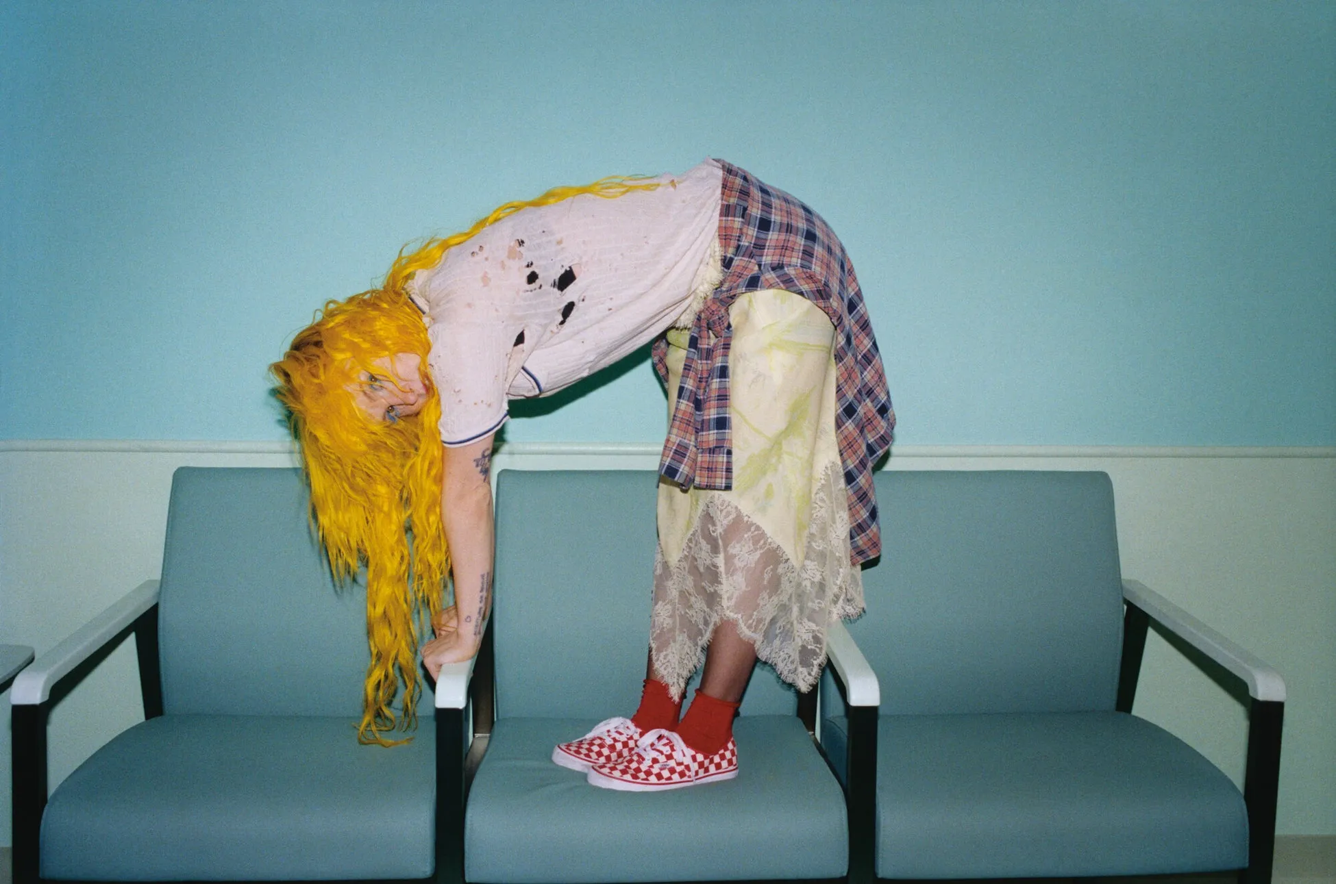 黄色い髪の女性が青い椅子の上で体を曲げる