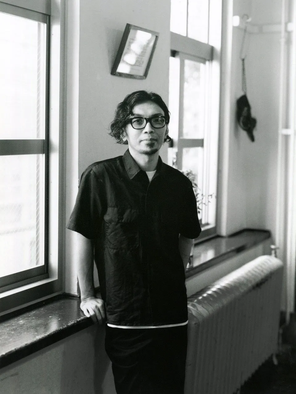 窓際に立つ男性のモノクロ写真 (サイトウユウスケ氏のポートレート)