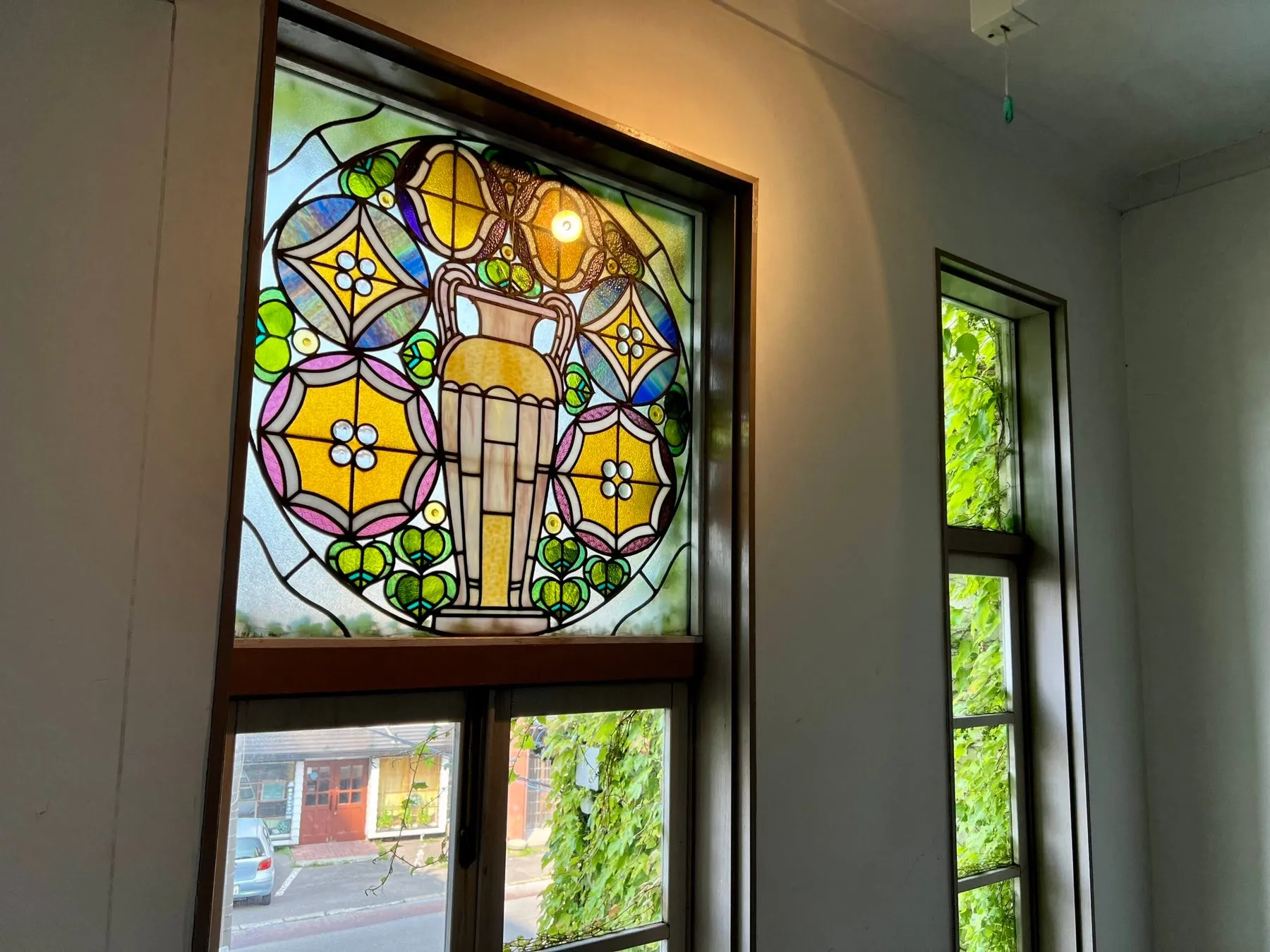 ステンドグラスが施された窓と、緑の葉が茂る窓が並んだ室内の写真。