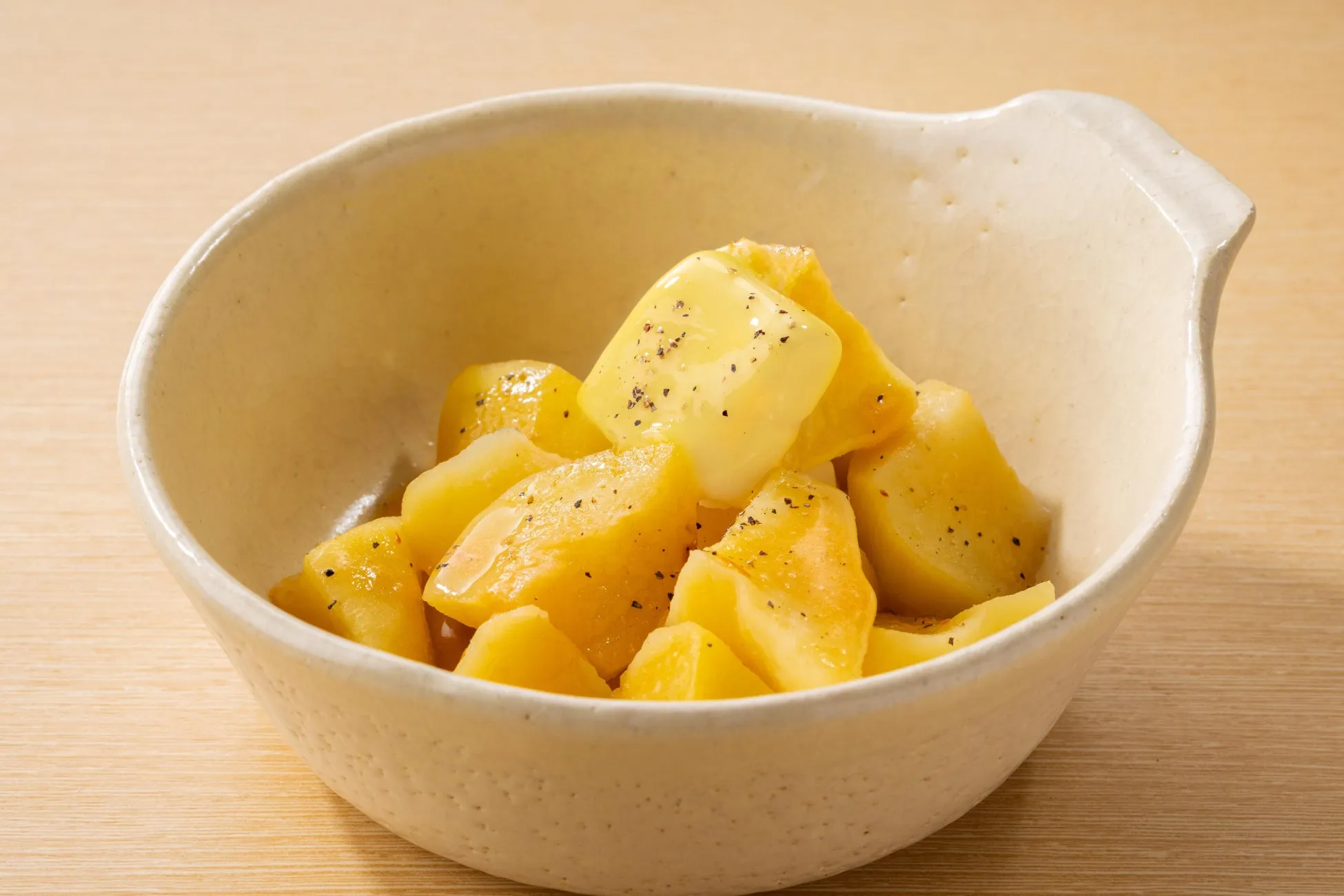 お皿に入った、黄色い角切りのジャガイモの料理の写真です。バターが乗っていて、黒胡椒が振られています。