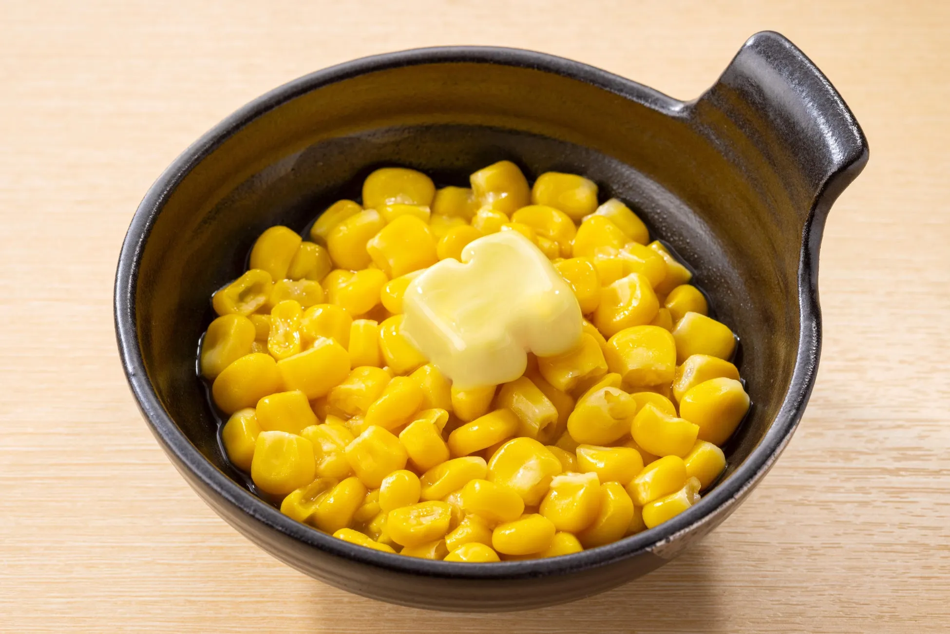 黒い器に入ったコーンとバターの画像です。コーンの上にはバターが乗っています。