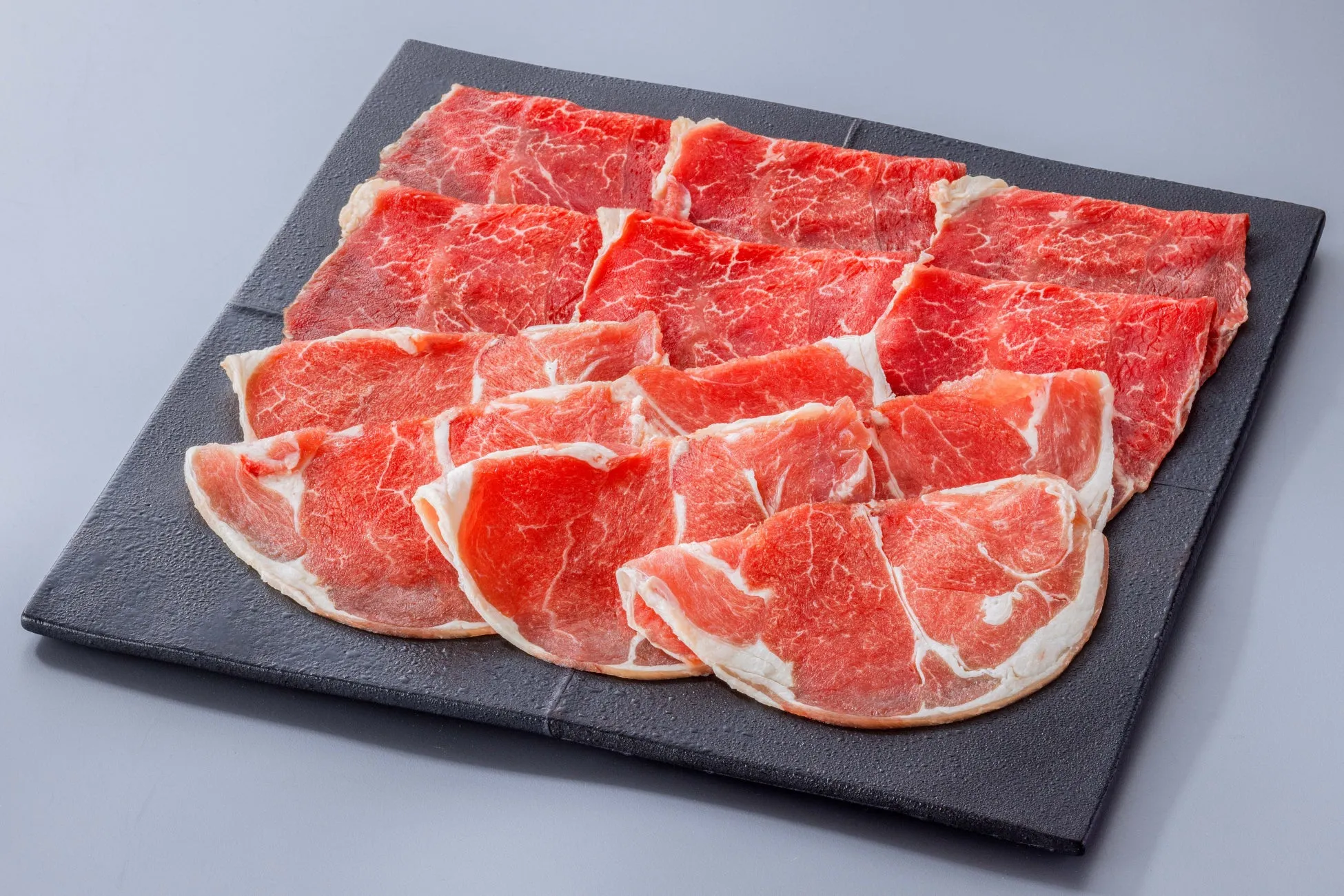 お皿に盛られた薄切りの赤身肉の写真。肉は赤色で、白い脂肪部分も見えます。