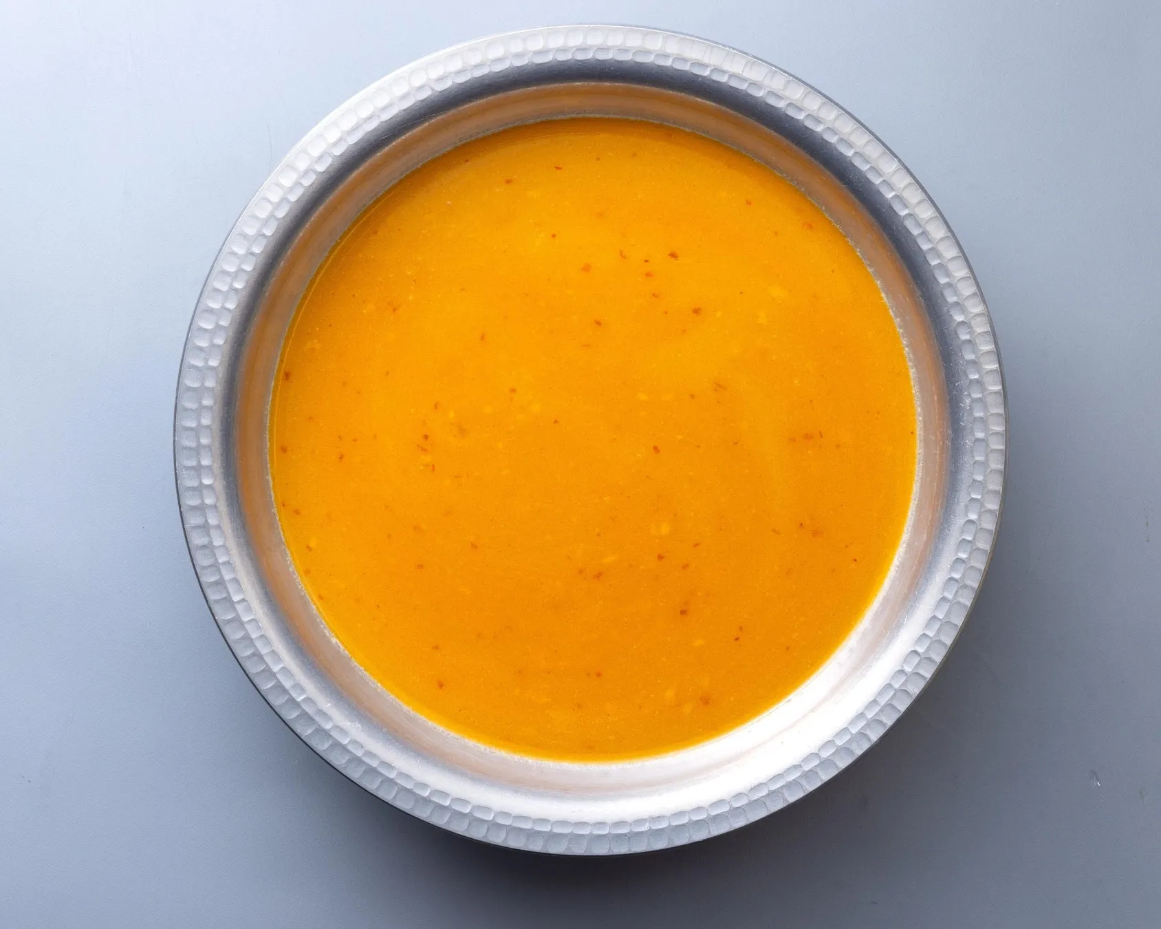 銀色の器に入ったオレンジ色のスープの俯瞰写真です。