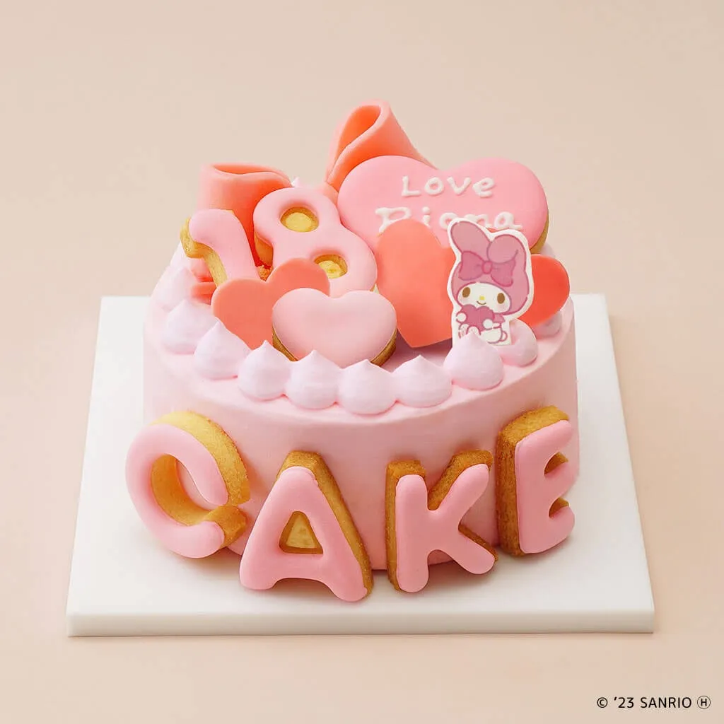 ピンク色のケーキ。上にはハートやキャラクターの飾り、側面にはCAKEの文字が施されている