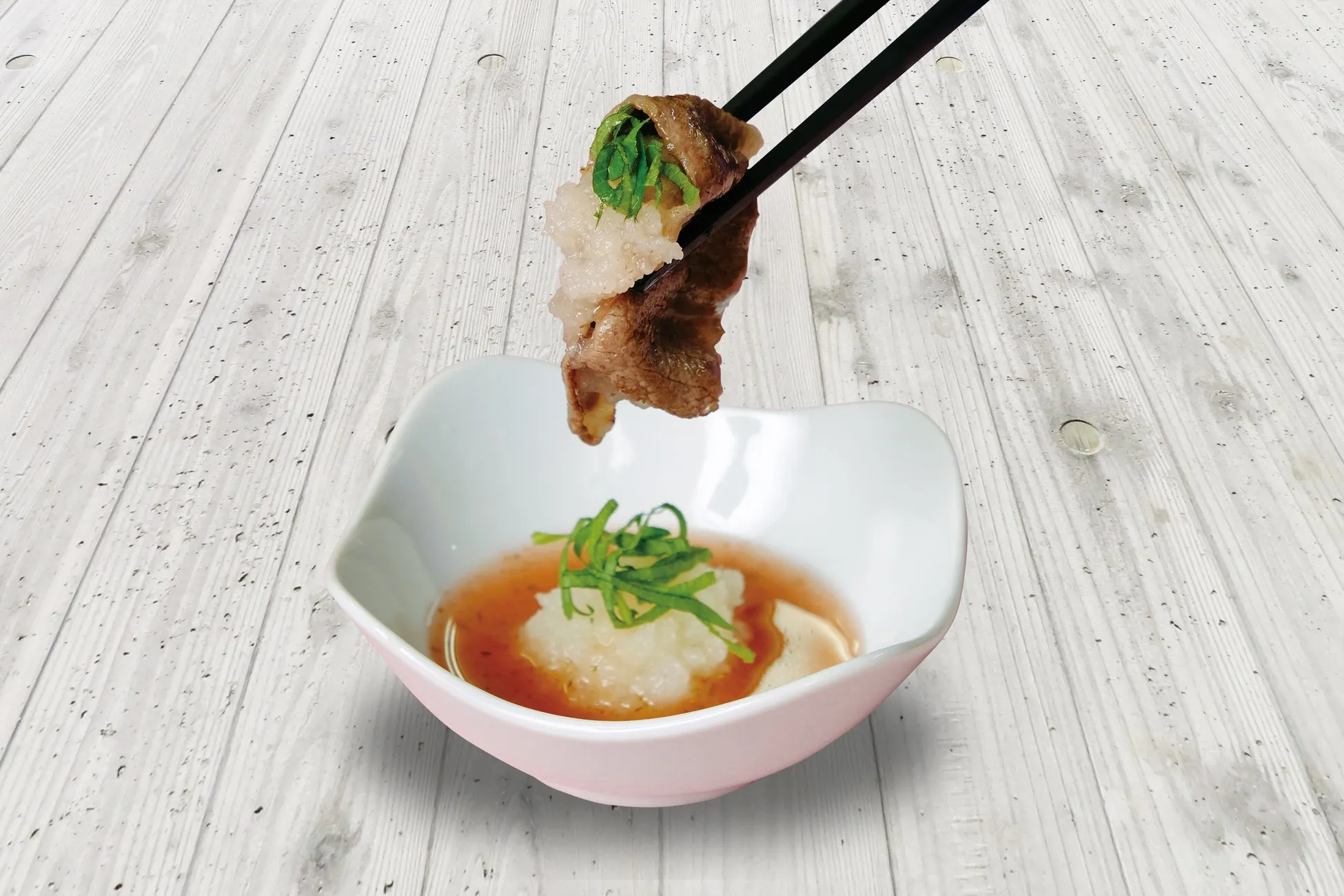 箸で持たれた牛肉の巻物と梅おろしダレ