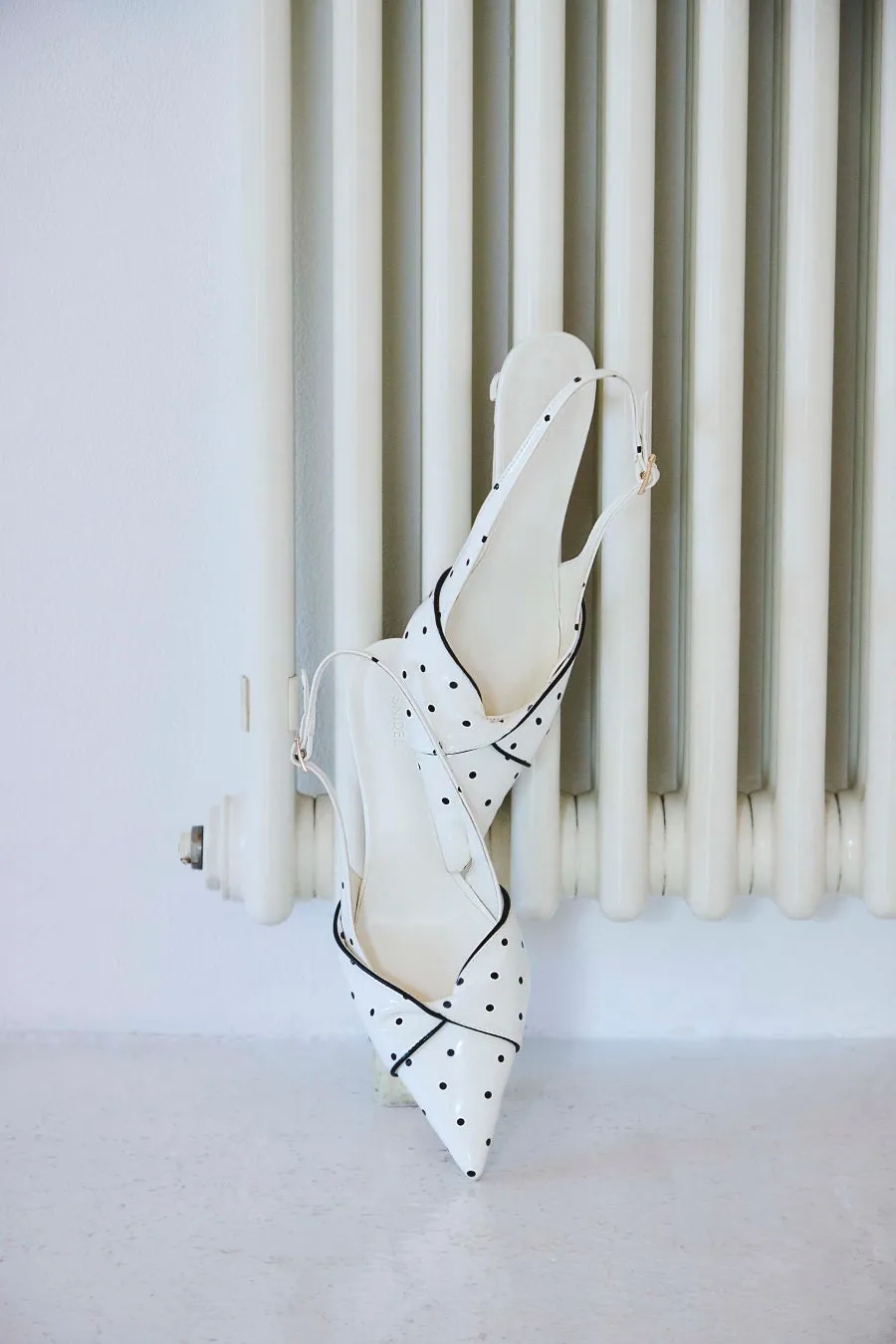 白い水玉模様のパンプスが、白い壁と白いラジエーターの上に置かれています。