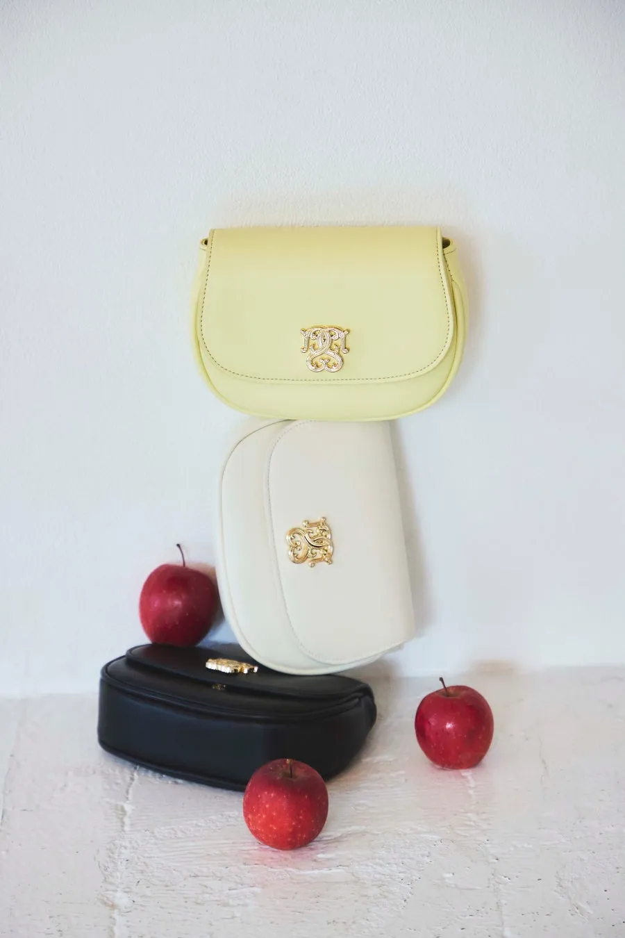 3つのバッグとリンゴが置かれた写真。黄色のバッグ、白いバッグ、黒いバッグが重ねて配置されています。