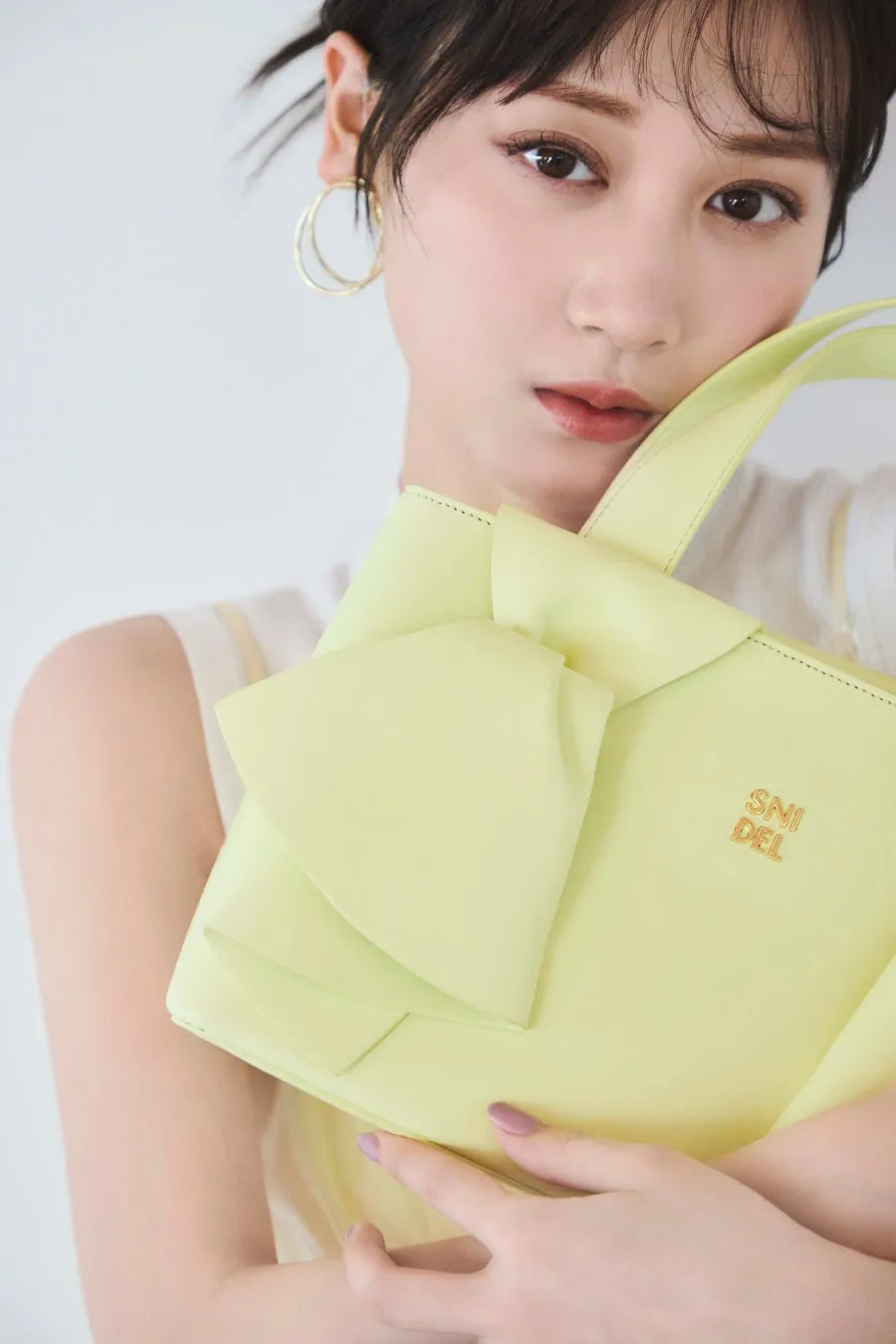 女性が黄色のバッグを持ち、カメラ目線で写っている写真。バッグには「SNIDEL」のロゴが見える。