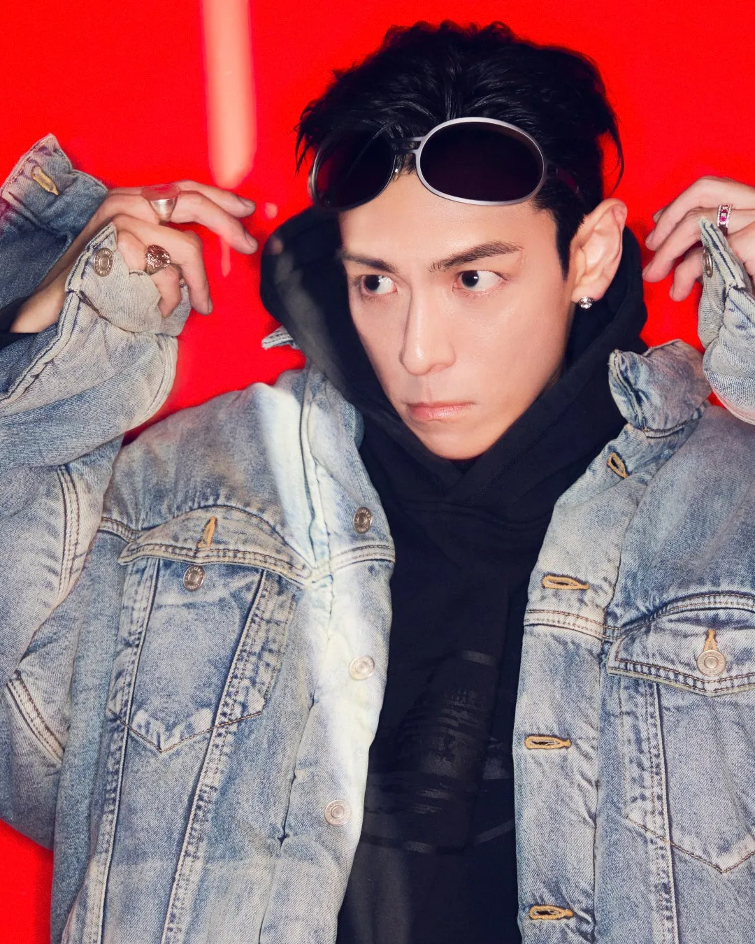 赤い背景に、サングラスをかけ、デニムジャケットを着た男性のポートレートです。