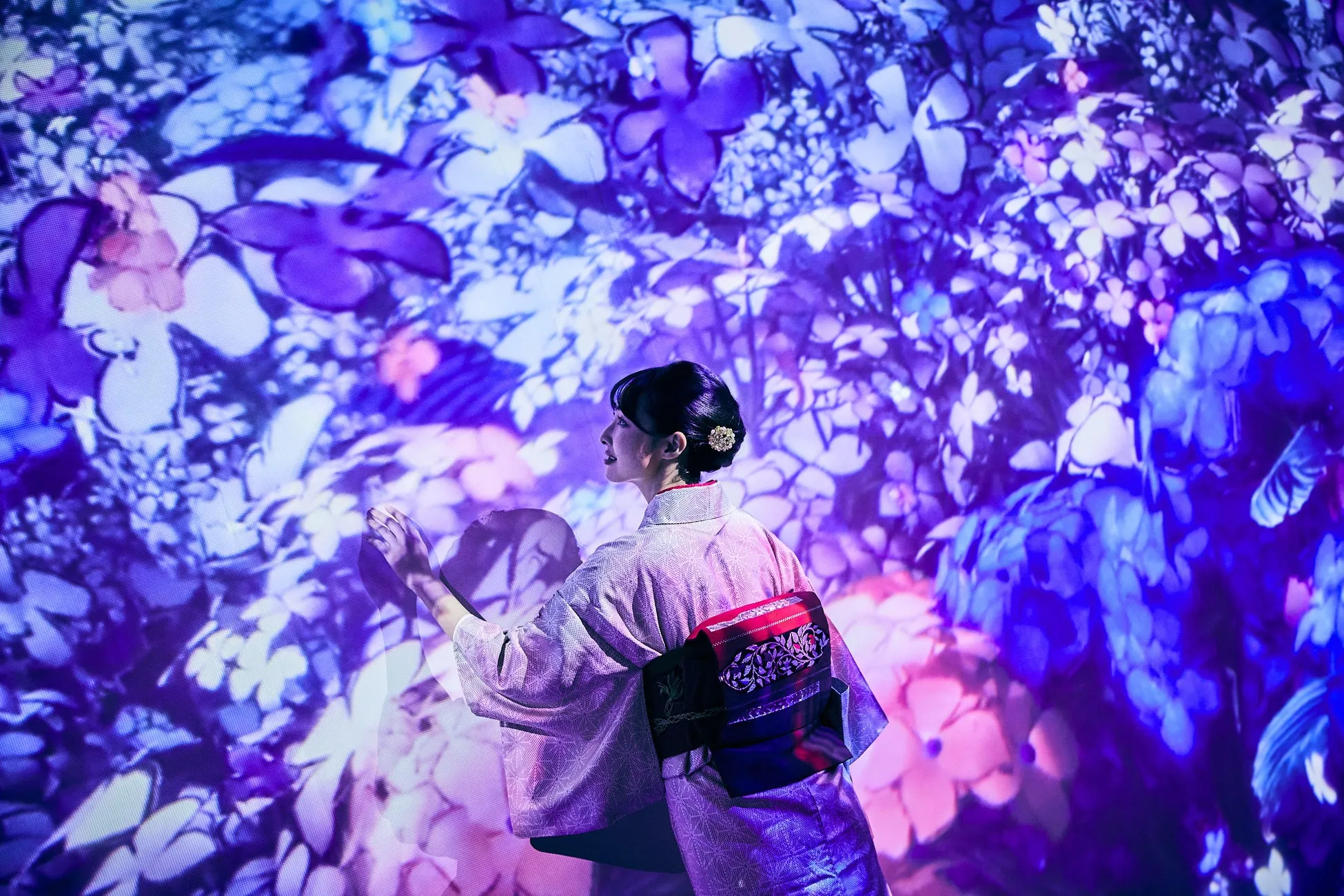 花が咲き乱れる空間で手を伸ばす着物姿の女性