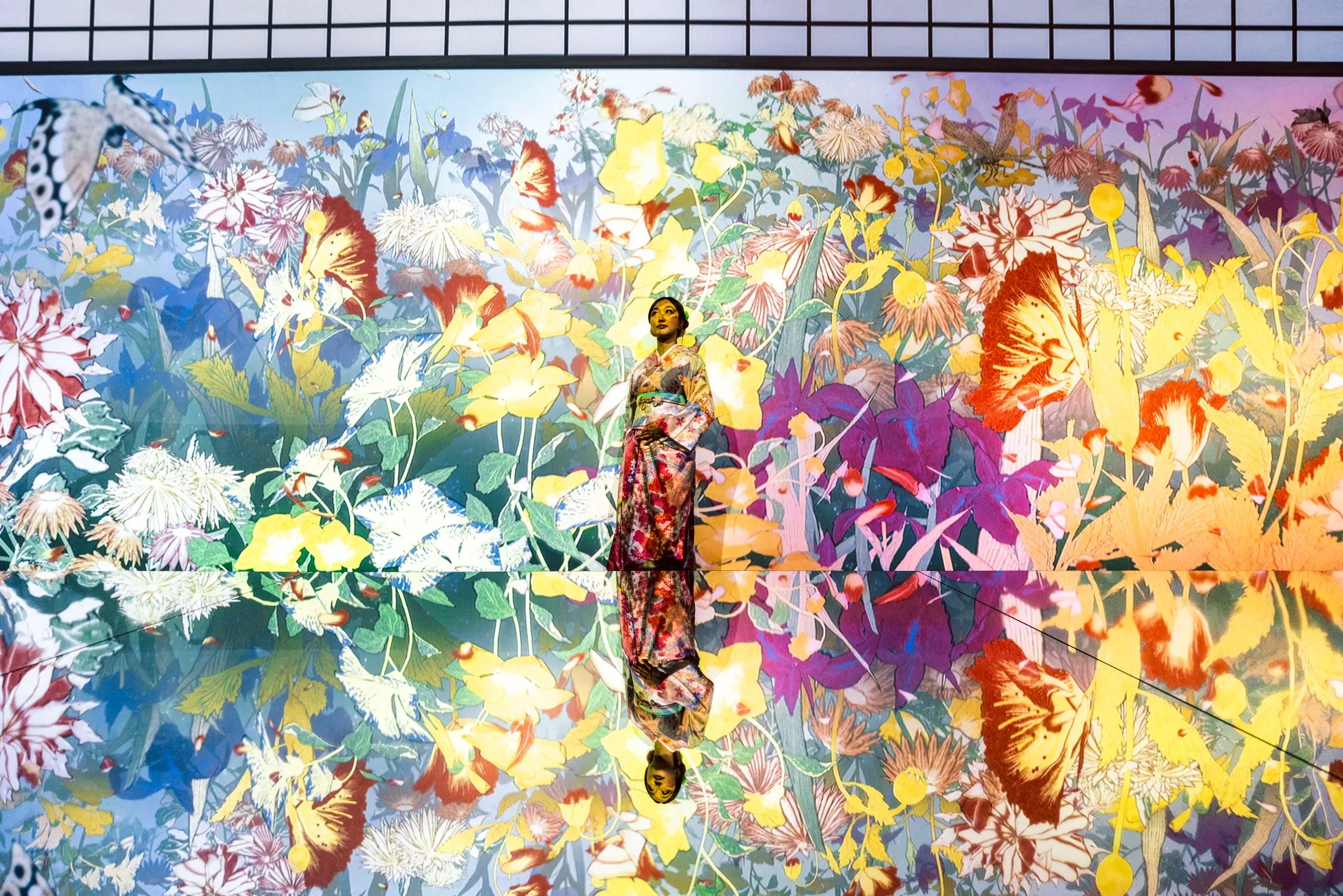 花や蝶が描かれた鮮やかな背景の前に立つ着物姿の女性