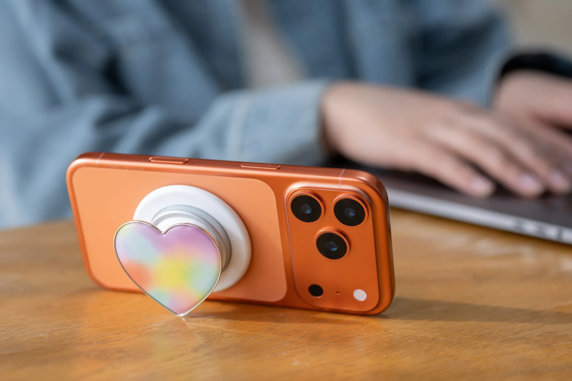 オレンジ色の携帯電話にハート型のスマホグリップが付いている様子。