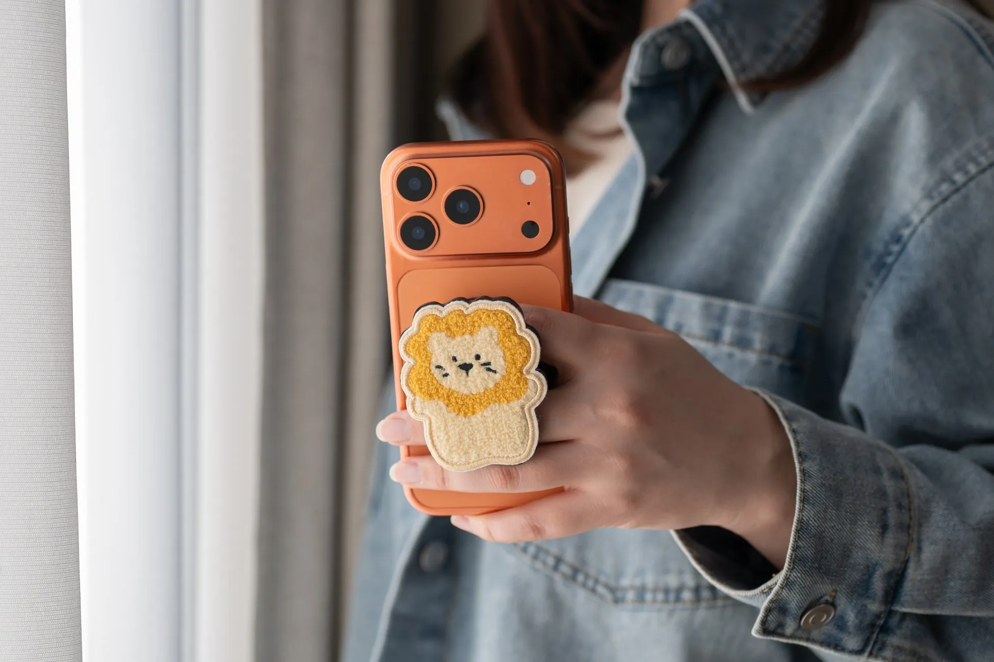 スマホを持った女性。スマホにはライオンの顔のグリップが付いている。