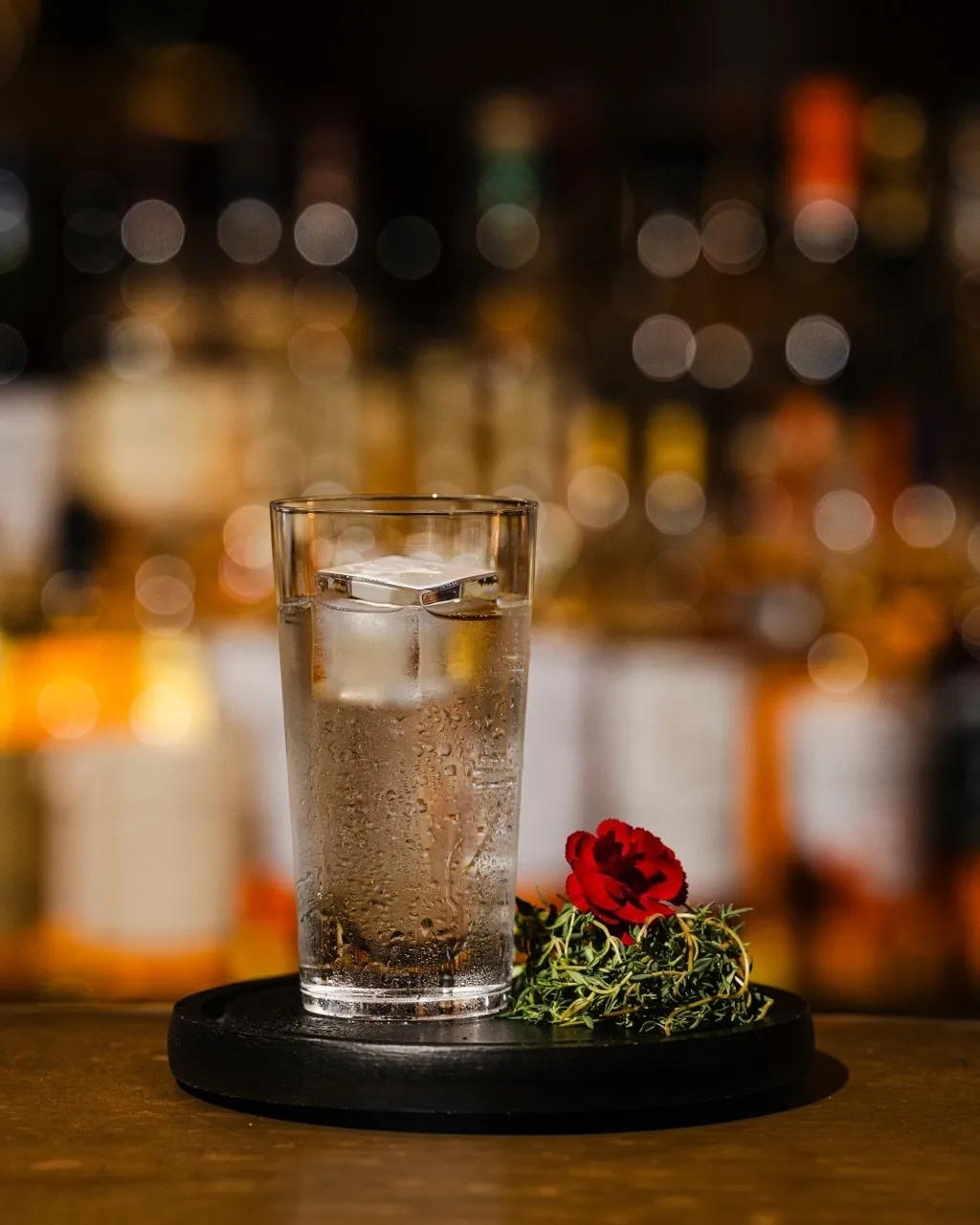 透明なグラスに入った飲み物と、皿に盛られたハーブと赤い花の写真