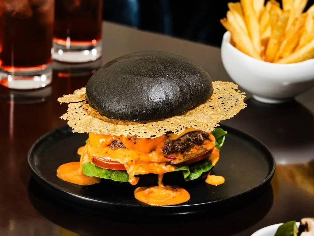 黒いバンズのハンバーガー、フライドポテト、ドリンクの画像。