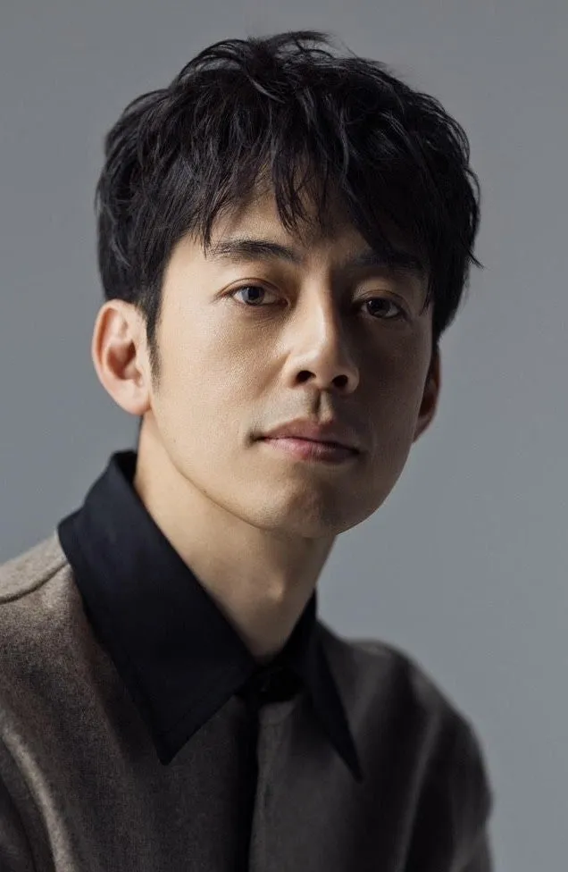 正面を向いた、黒髪の男性のポートレート。男性は黒い襟付きの服を着ています。