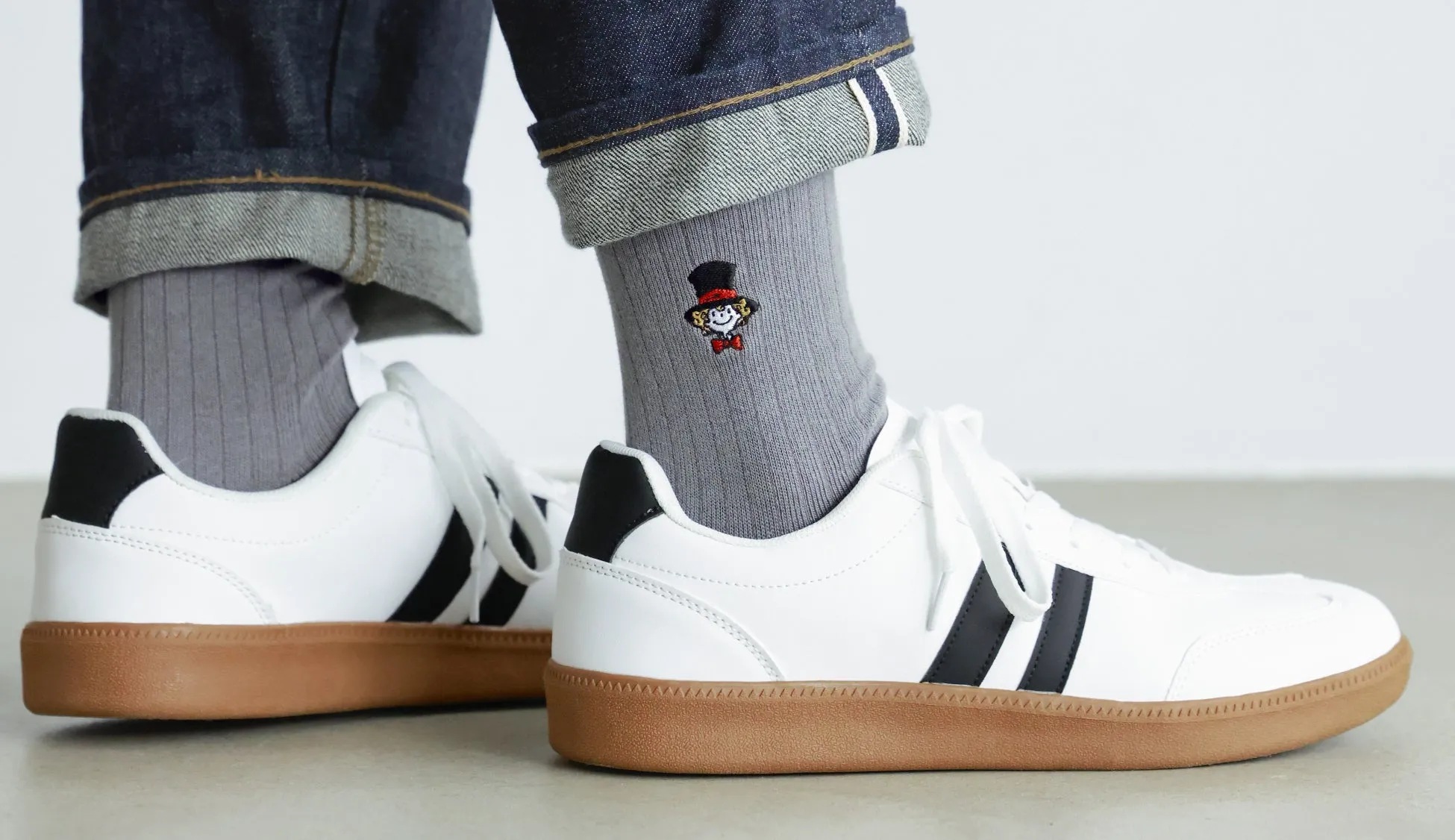 白と黒のスニーカーとグレーの靴下を履いた足元の写真。靴下には小さなキャラクターの刺繍が施されている。