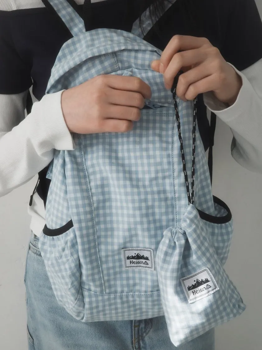 水色のチェック柄のリュックサックと巾着を持っている女性の画像です。リュックサックには「Heisen」のロゴが入った四角いパッチが付いています。
