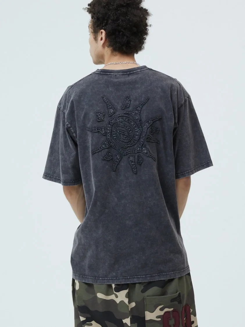 男性が後ろを向いて立っており、背中には太陽の刺繍が施された黒いTシャツを着ています。