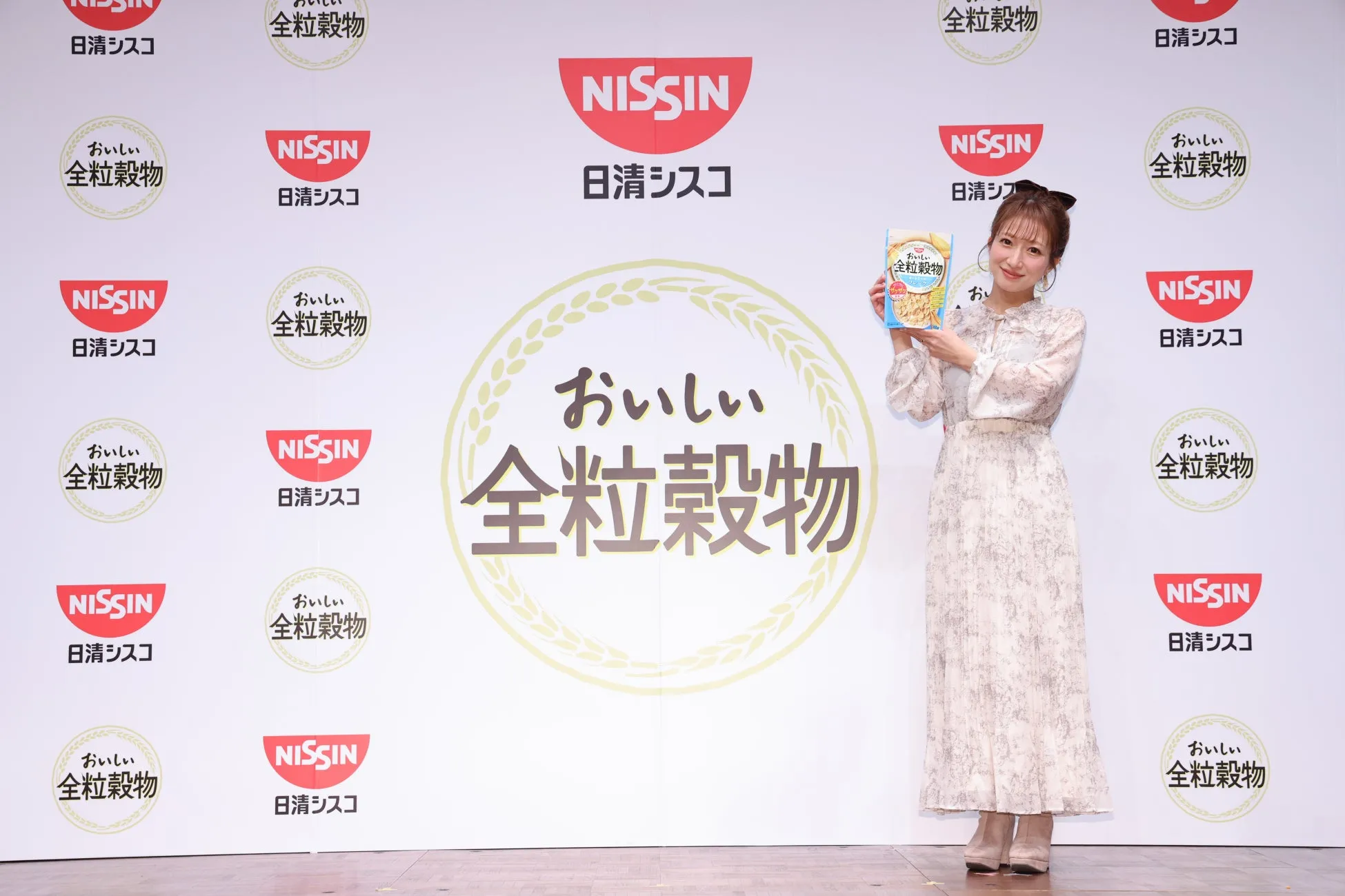 女性が「日清シスコ」の「おいしい全粒穀物」のパッケージを持って立っている写真です。