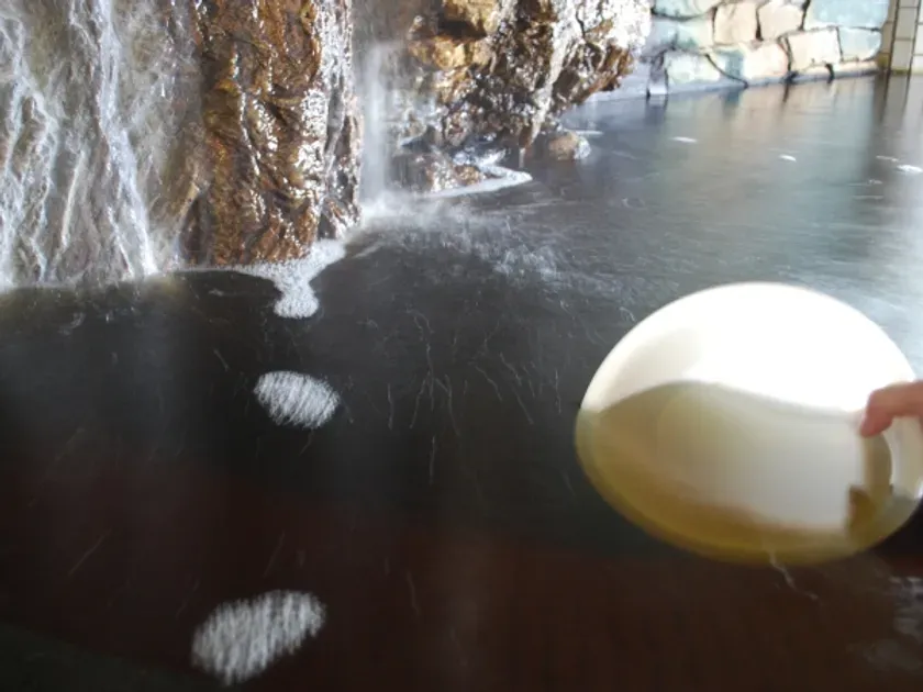滝のある温泉の風景。温泉水面には泡が立ち、手には器が持たれている。