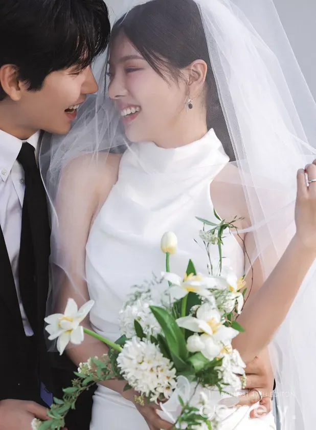 新郎新婦が寄り添い、幸せそうに微笑んでいるウェディングフォト。新婦は白いウェディングドレスとベールを身につけ、ブーケを手にしている。