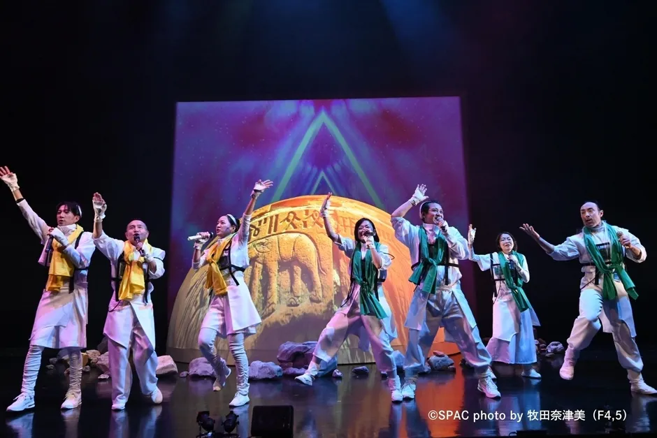 舞台上で歌い、手を上げる衣装を着た人々。