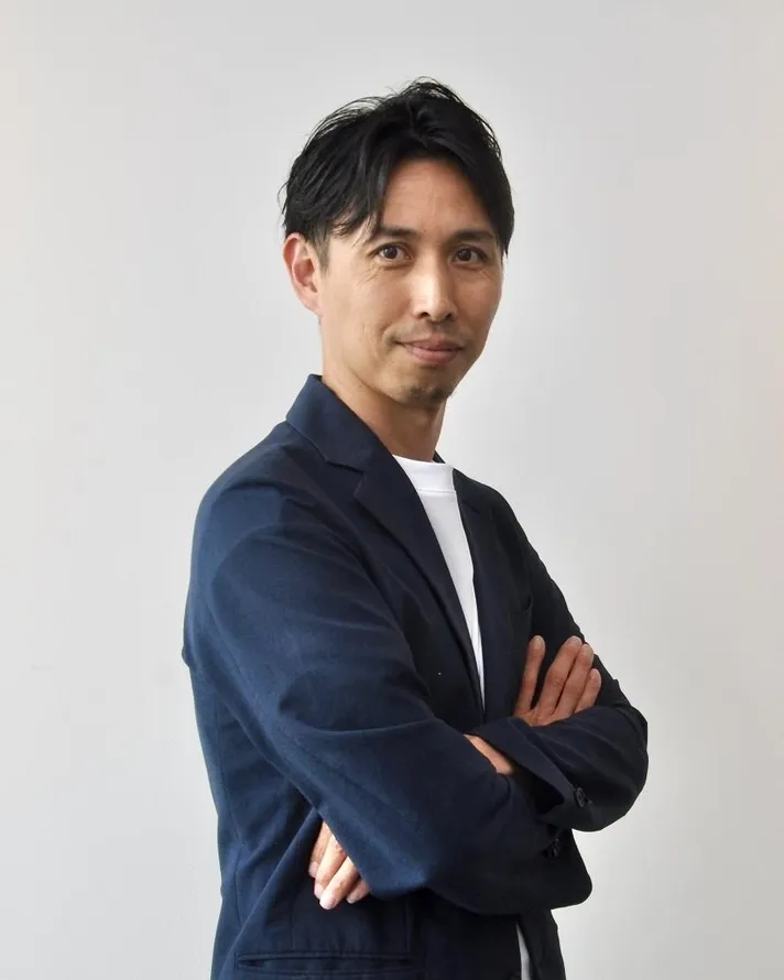 腕組みをしてカメラ目線で微笑む男性のポートレート。