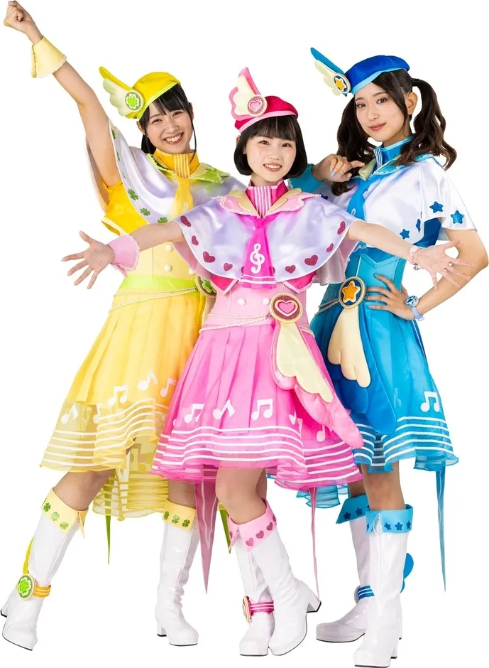 3人の女性が、それぞれ黄色、ピンク、青の衣装を着てポーズをとっている写真。