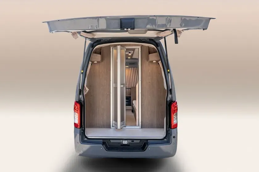 キャンピングカーの後部ドアが開いた状態の画像。内装は木材で、シャワーブースのような仕切りが見える。