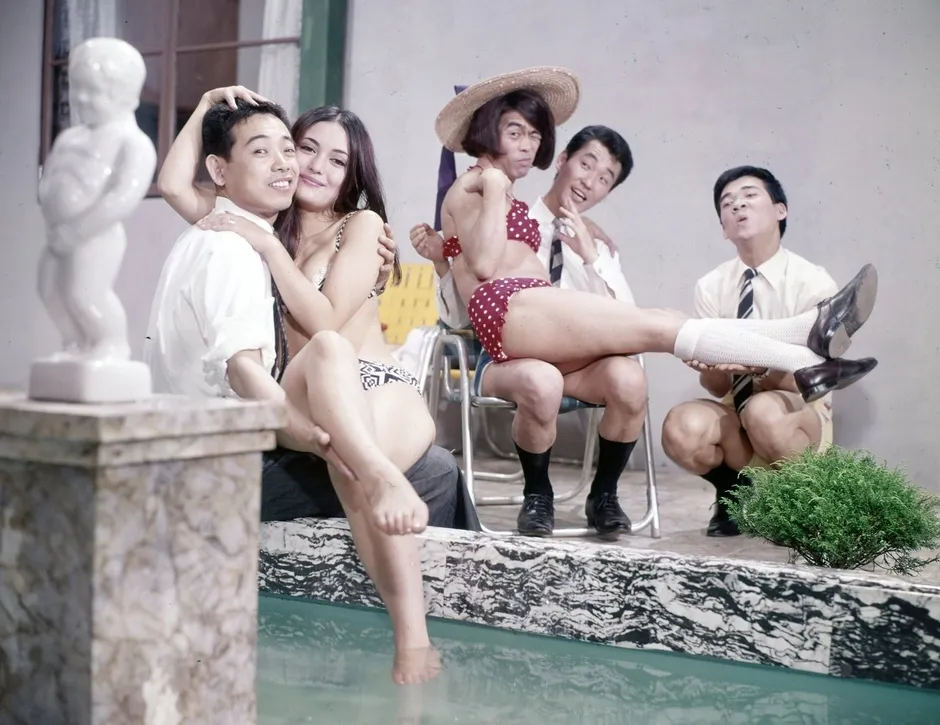 プールサイドで楽しむ6人の人々の写真。女性2人がビキニ姿で、他の男性たちは面白いポーズをとっている。全体的にユーモラスで、リラックスした雰囲気。