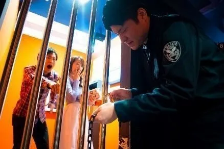 警察官が牢屋の鍵を開けようとしている様子を、2人の人物が驚いた表情で見ている様子。