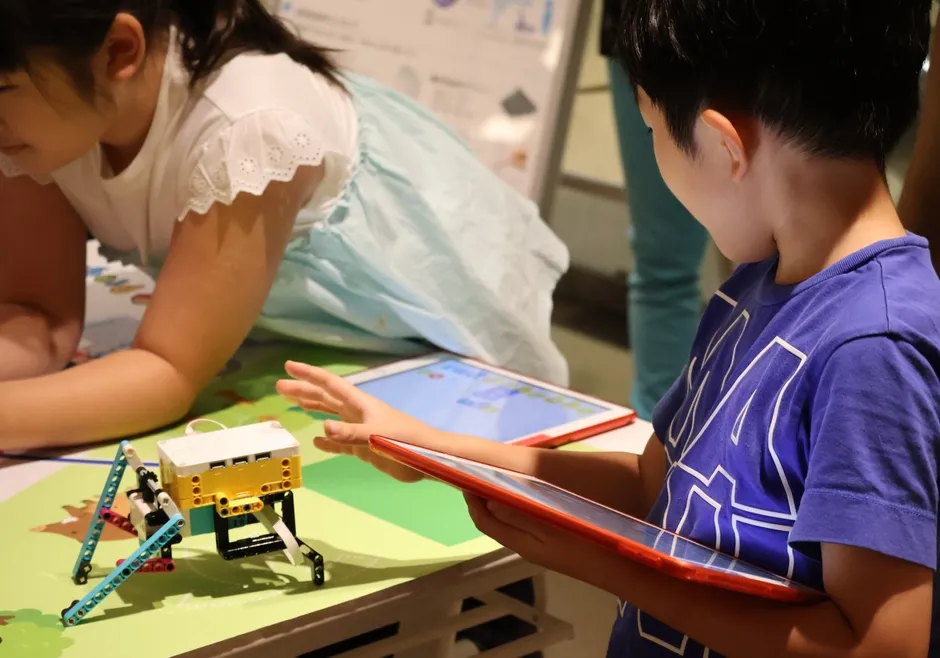 子どもたちがタブレットを操作してロボットを動かす様子