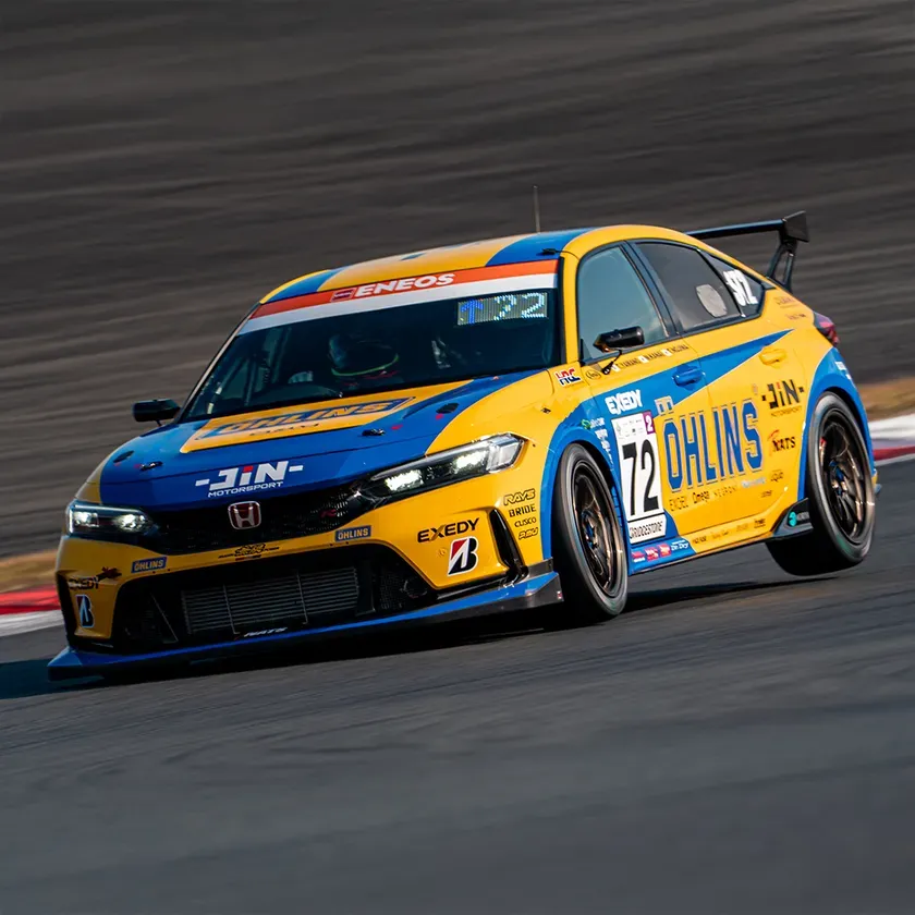 サーキットを走行する黄色と青色のレーシングカー。車体にはスポンサーのロゴや数字が描かれている。